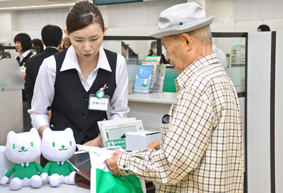 高齢者にも伝票に記載しないでタブレット端末による取引を促す行員（6月19日、埼玉りそな銀行鶴瀬支店）＜ニッキン7月7日号4面＞