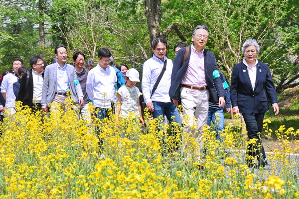 菜の花が満開となった「埼玉りそなの花壇」の前をハイキングする行員たち。(４月22日、先頭は池田社長と大澤町長)