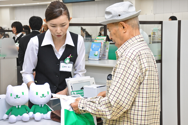 高齢者にも伝票に記載しないでタブレット端末による取引を促す行員。(６月19日、埼玉りそな銀行鶴瀬支店)