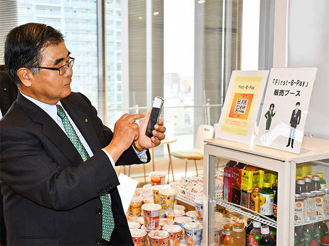 無人販売所でスマホアプリの使い方をデモンストレーションする横田頭取（１１月２８日、本部ビル）