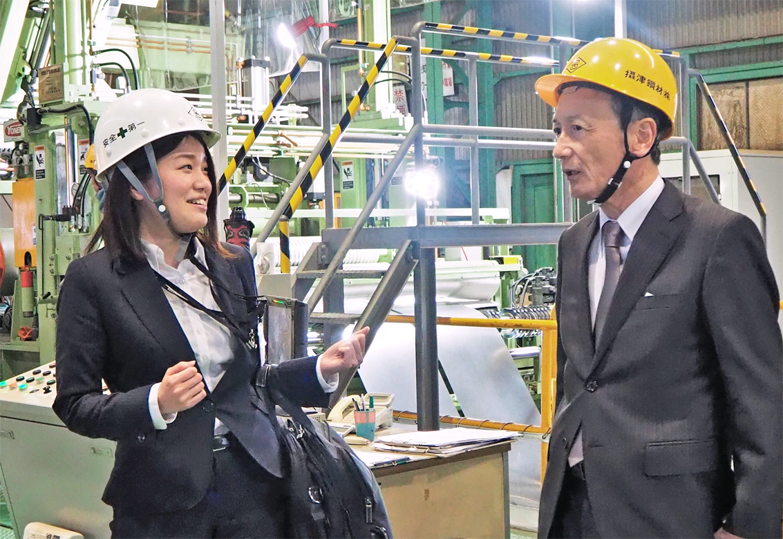 摂津鋼材の長谷川修(右)から工場設備や作業工程を聞く南都銀行大東支店の女性担当者(2月4日)