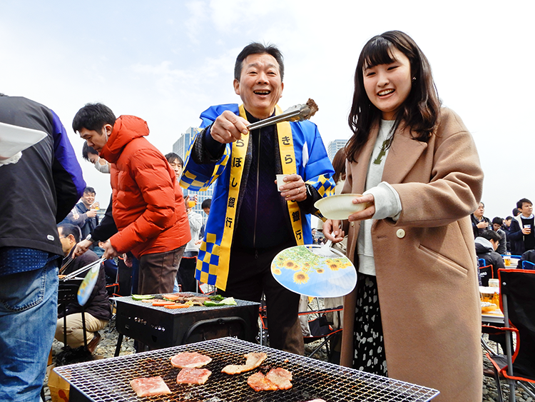 バーベキューで焼いた肉を行員に配る渡邊頭取(3月16日、川崎市多摩川緑地)