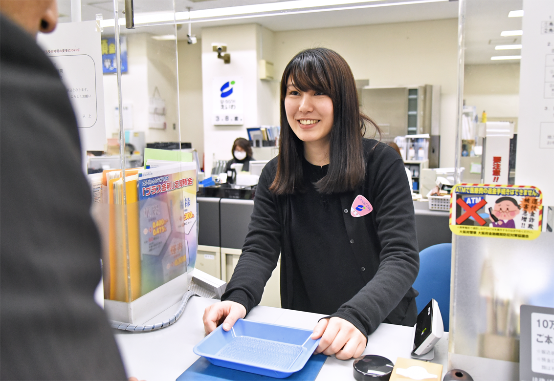 カジュアルデーの専用バッジを付けて窓口対応する本店営業部の担当者（３月８日、永和信用金庫本店）