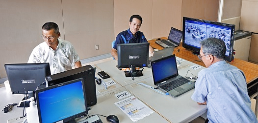 琉球銀行のコザサテライトオフィスには、シンクライアント対応のパソコン４台のほか、本部各部と双方向に視認・閲覧できるモニターとカメラを整備（2018年７月31日）