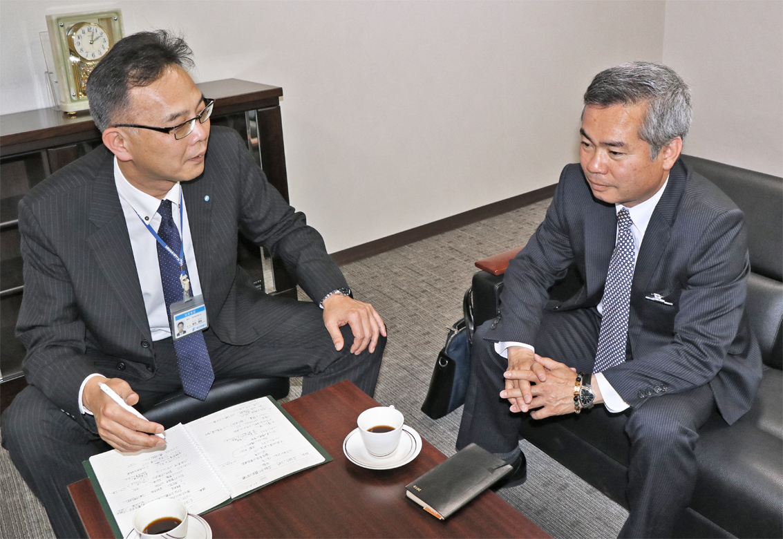次男への介護事業の承継を検討している緑陽の会緑ヶ丘グループ・新田裕造会長(右)と面談する鮫島統括調査役(4月1日、南日本銀行本部)