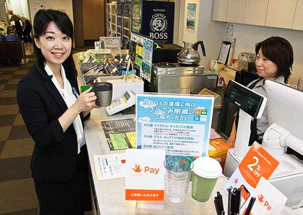 マイカップを持参してコーヒーを注文する藤谷さん（左、７月２９日、本店）