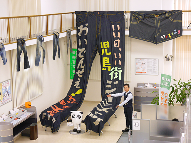 大型タペストリーやパンツ、小物類で店内を装飾。青木支店長も新調したデニム製品に身を包みPR(10月23日、児島支店)