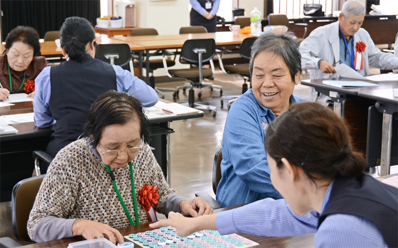 教室サポーターの補助を受けながら、教材の一つ「すうじ盤」でトレーニングする参加者(10月25日、玉島信用金庫本店)