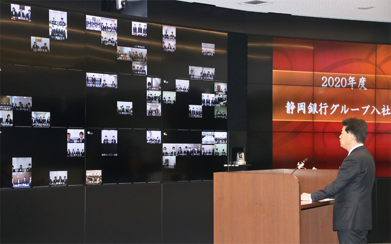 静岡銀行グループ入社式で、非常事態対策室のテレビ会議システムを通じてメッセージをライブ配信する柴田久頭取。本部で辞令交付を受けた新入社員代表を除く新入社員は配属店など48カ所に分かれ、各店のモニターを通じて参加した(4月1日、静岡銀行本部)