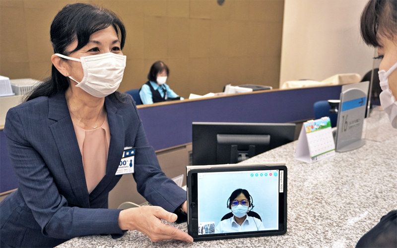 外国人客はタブレット端末の映像通訳を見ながら、行員から手続きやサービスの案内を受ける(5月28日、横浜銀行本店営業部)