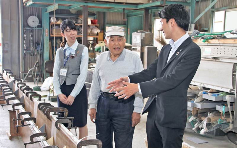 工場で製品を前に鈴木樹脂工業の鈴木雅二代表取締役（中央）と談笑する、清水銀行吉原支店のマネーアドバイザー（左）、渉外係（６月５日）＜写真撮影時にマスクを外していただきました＞