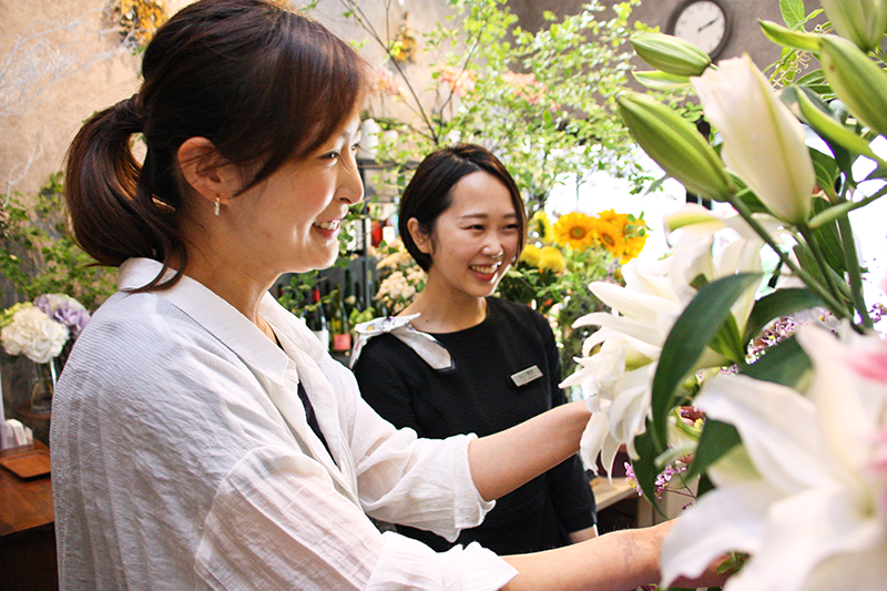 巣鴨信金の谷口さん(右)に季節の花を説明する堀野さん。産地や品種にこだわる(7月16日、ジフィー)