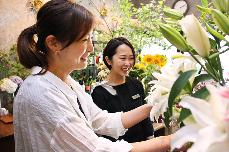 巣鴨信金の谷口さん（右）に季節の花を説明する堀野さん。産地や品種にこだわる（7月16日、ジフィー）