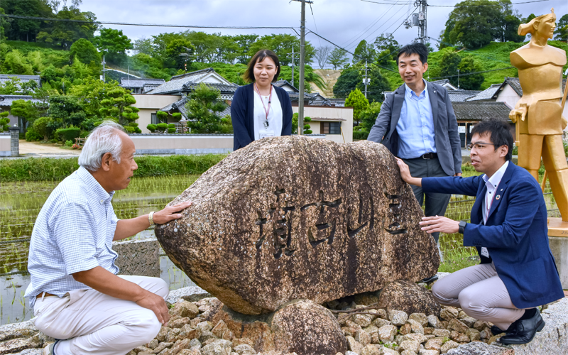 古墳前でクラウドファンディングのリターンを相談する（左から）定廣好和・造山古墳蘇生会会長、窓口係の女性行員、能登弘幸・稲荷支店長、野田映博・稲荷支店長代理（７月１日、岡山市）