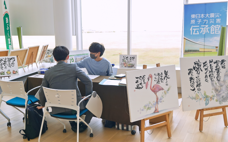 あぶくま信金が紹介した会場の一角で訪れた人に「ことば絵」を描く新井氏(奥、11月1日、東日本大震災・原子力災害伝承館)