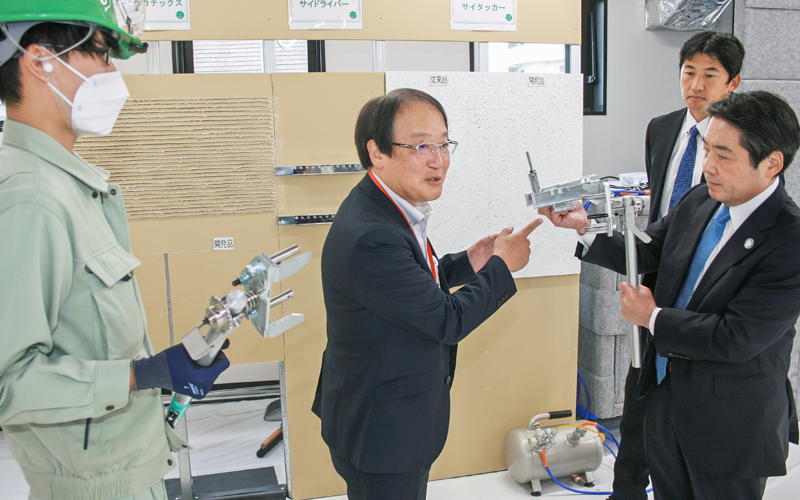 丸高工業の高木一昌社長(右)から騒音や振動のない工具の説明を受けるきらぼしコンサルティングの強瀬理一社長(左から2人目)