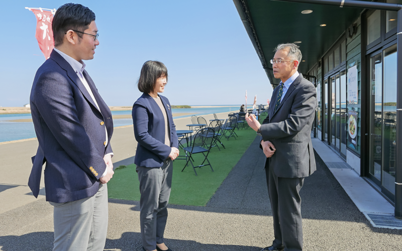 櫻井広行・かわまちてらす閖上代表(右)と談笑する鈴木恭子支店長(中央)と担当者(3月9日、「かわまちてらす閖上」前)