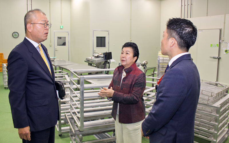 海連の永井幸枝代表取締役（中央）から芋の加工設備について説明を受ける菊永栄一郎常務執行役員支店長（左）と同社の担当者（３月２４日、海連阿久根工場）