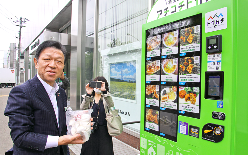 「ホエー豚ぎょうざ20個」を購入した高橋常夫理事長(左、6月8日、帯広信用金庫本店)