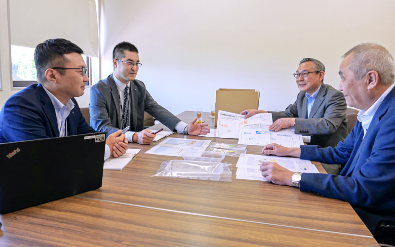 笹原真社長(右手前)と総務部長(右から2人目)に説明する部長代理(左から2人目)と課長(6月14日、成邦商事)