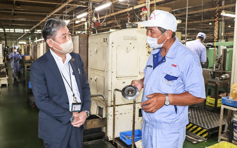 中日精工の山本哲司社長（右）からトラクター用ギアの製造法を聞く山口朝昭支店長（８月23日、中日精工）