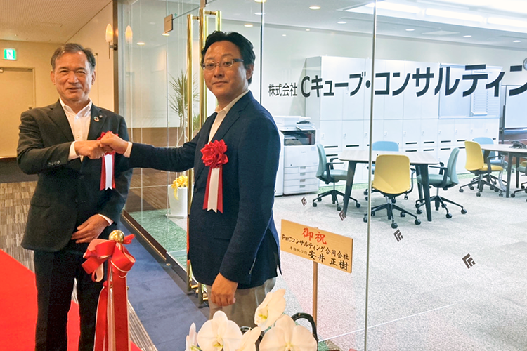 Cキューブ・コンサルティングのオフィスの前で拳を合わせる加藤頭取(左)と西原社長(9月1日、岡山市)
