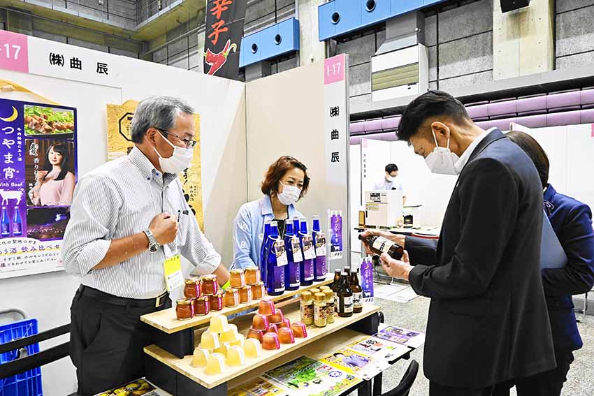 ビジネス交流会の会場で、開発したビールなどを紹介する曲辰の森廣専務(左、岡山市内、9月14日)