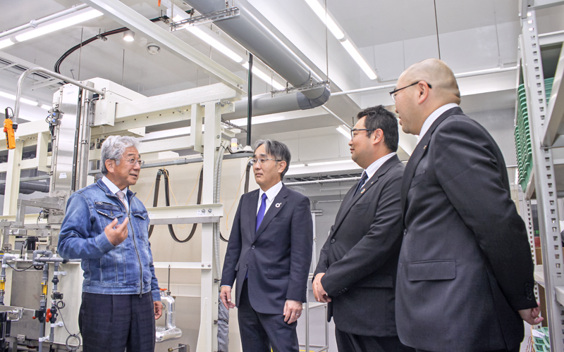 高木治邦代表取締役(左)から新工場の稼動状況を聞く花畑晃洋支店長(左から2人目)ら(11月24日、マイクロカット第9工場)