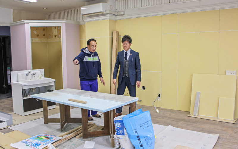 豪雨で被災した有限会社やまたきの山田俊治郎代表取締役(左)と今後の対応などについて話し合う渡部良支店長(1月17日、復旧工事中の同社店舗)