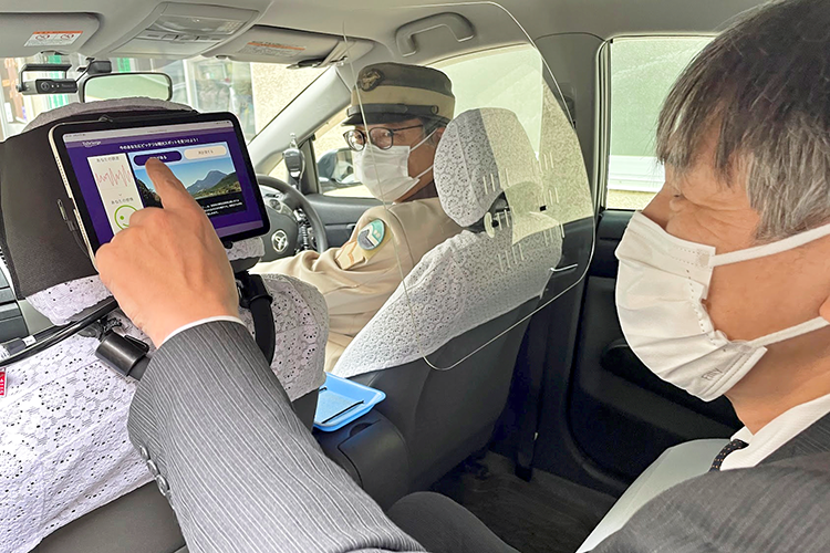 観光タクシーの後部座席に搭載したタブレット端末で感情計測装置を操作する乗客（3月24日）