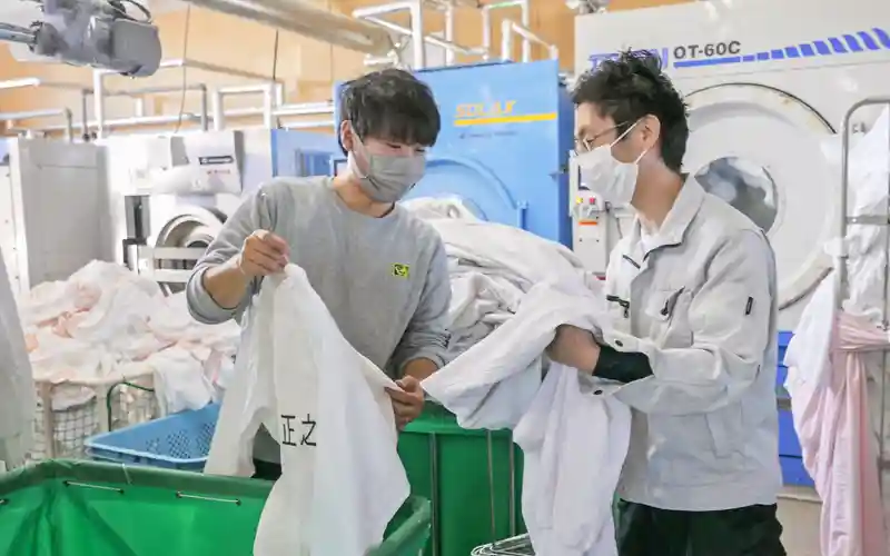 佐藤光工場長（右）から作業の指導を受ける担当者（12月６日、トータルクリーニングサービスたこい）