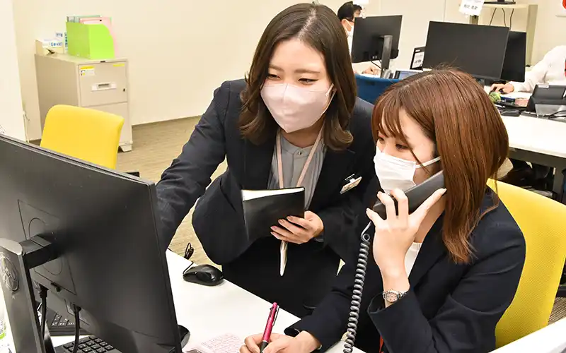 野村証券のコンタクトセンターで2022年8月から7カ月間、研修を受けた山陰合同銀行の米子コンサルティングプラザの秦野真美さん(左)は学んだノウハウを若手に伝えている(2023年12月13日、山陰合同銀行の米子コンサルティングプラザ)