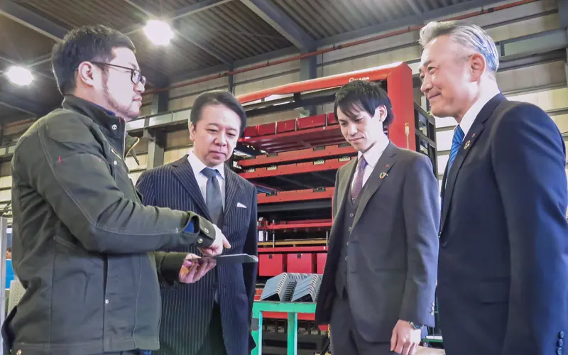 富永スチール工業の富永崇仁取締役工場長(左)と富永健治社長(同2人目)から説明を受ける担当者(同3人目)と松尾隆寛支店長(2月29日、富永スチール工業)