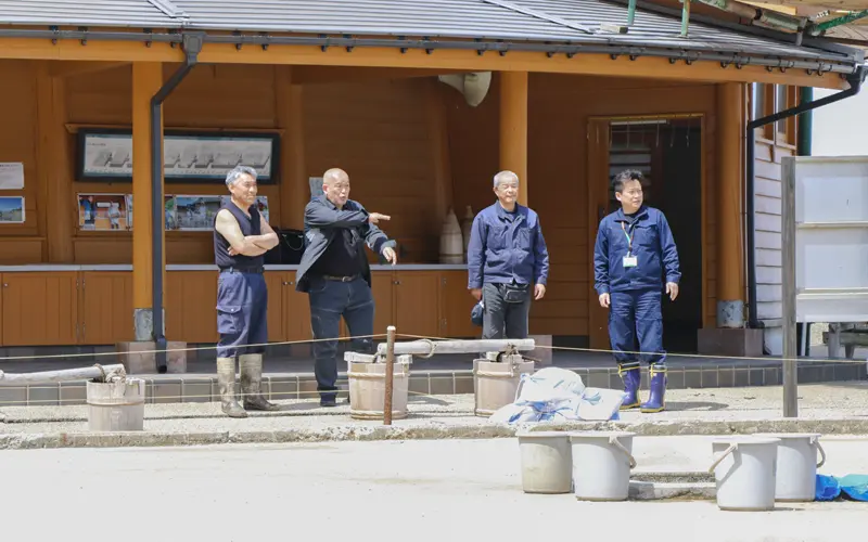 塩田村の状況を説明する石田尚史社長(左から3人目)と中野文彦・興能信金珠洲支店長(同4人目、4月19日、奥能登塩田村)