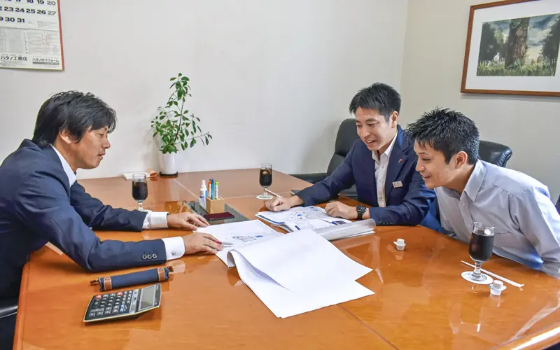 取引先のハタノ工務店の佐藤実専務(左)と打ち合わせする佐藤智紀支店長(中央)と吉澤謙太お客様サービス課長(7月10日、ハタノ工務店)
