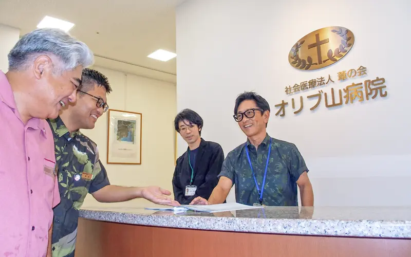 葦の会オリブ山病院の仲本賢一郎常務(右)と仲本悠輝法人事業統括室課長(右から2人目)にソリューションを提案する古波蔵英樹支店長(左)と島袋宏一副長(11月15日、オリブ山病院)