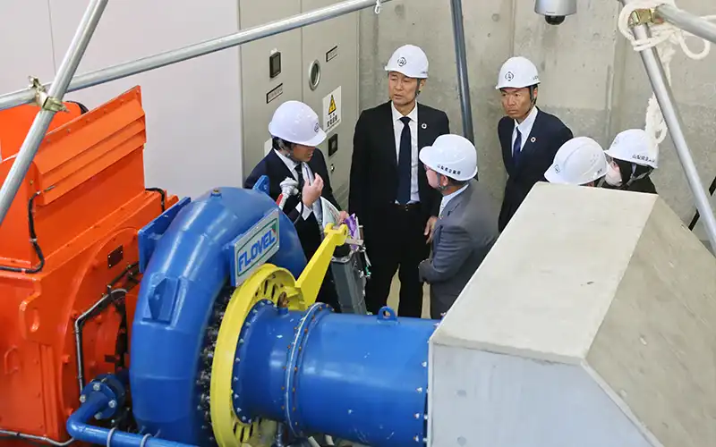 県担当者(左)の案内で重川発電所の設備を見学する行員ら(2月26日、山梨県甲州市)