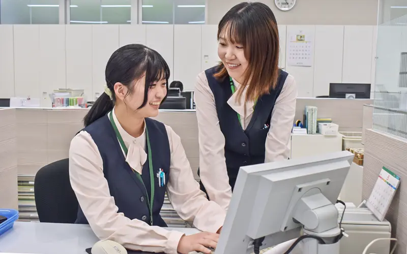 預金係の先輩(右)から事務作業を学ぶ女性職員(5月9日、千葉信金誉田支店)