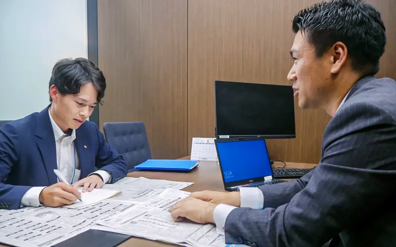 野村証券からの出向者である佐藤雄大経営役（右）と新聞の読み合わせを行う阿波銀行担当者（６月26日、徳島コンサルティングプラザ）
