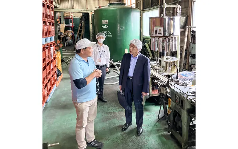 事業参加者（手前左）に製造工程を聞く同信金職員（中央）と食品アドバイザーの寺谷健治氏（右、10月21日）