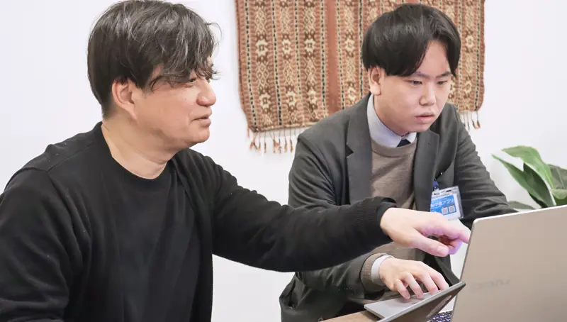 共同制作したサイトを確認する飯塚陽一・システム統括部主任調査役（左）（１月６日、山梨中央銀行本店）