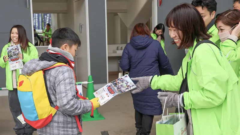 ホーム戦で預金チラシを配布する筑後信金の職員（2025年12月21日、久留米総合スポーツセンター陸上競技場）