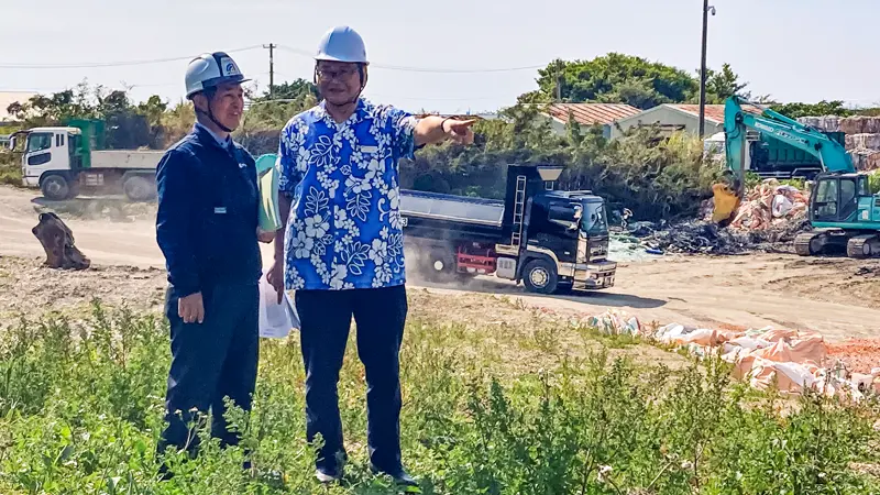 取引先幹部（左）から新施設建設の説明を受ける金子公洋支店長（３月18日、南城市内の新施設予定地、琉球銀行提供）