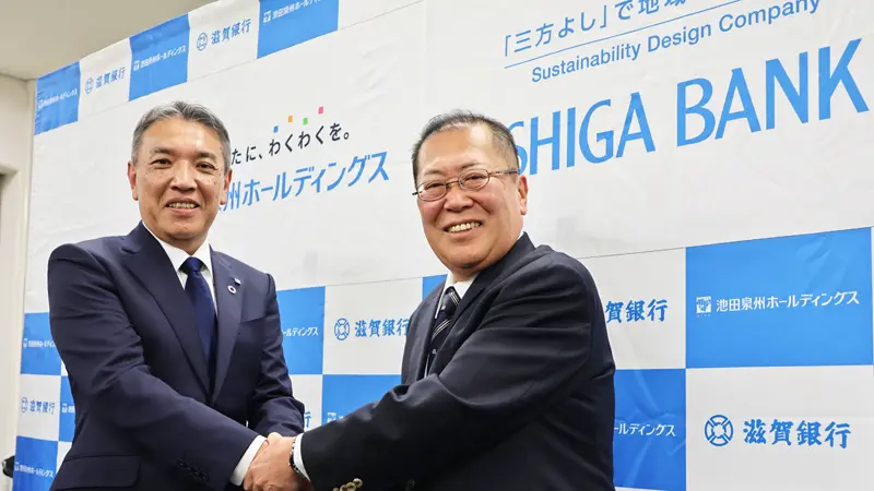 握手する阪口広一・池田泉州HD社長（左）と久保田真也・滋賀銀行頭取（４月17日、日本銀行大阪支店）