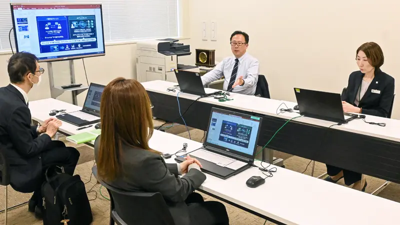 日常業務での生成AIの活用方法を説明する総合企画部の上野公彦参事役(左から3人目、4月21日、北おおさか信金本店)