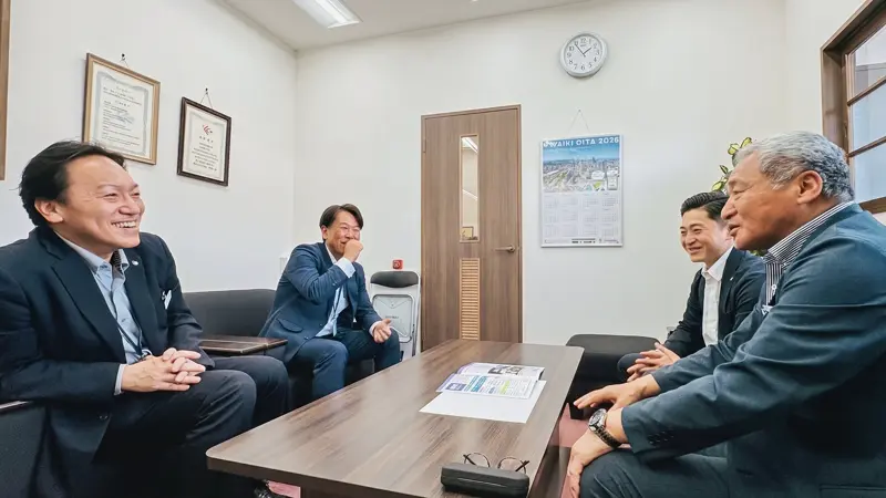 進捗（しんちょく）を伝える佐藤功宏社長（右）と佐藤大喜専務（右奥）、話を聞く別府支店の久留嶋彰夫支店長（左）と法人ソリューション部の中野和宜副部長（５月15日、大分県信組別府支店）