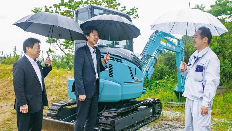 西本和寿・西本建設社長(右)から重機の説明を受ける担当者(中央)と佐藤浩樹支店長(5月19日、福島県広野町)
