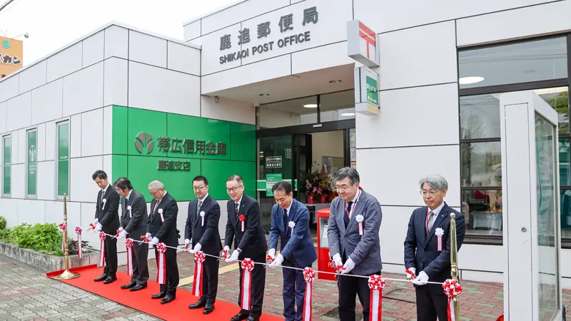 帯広信金鹿追支店と鹿追郵便局の支店併設記念セレモニーでテープカットする帯広信金の中田真光理事長（左から４人目、５月18日、帯広信金提供）