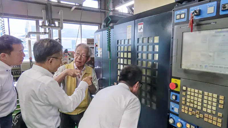 電気通信機器・通信部品製造業の社長(奥)から説明を聞く職員(さいしんコラボ産学官提供)